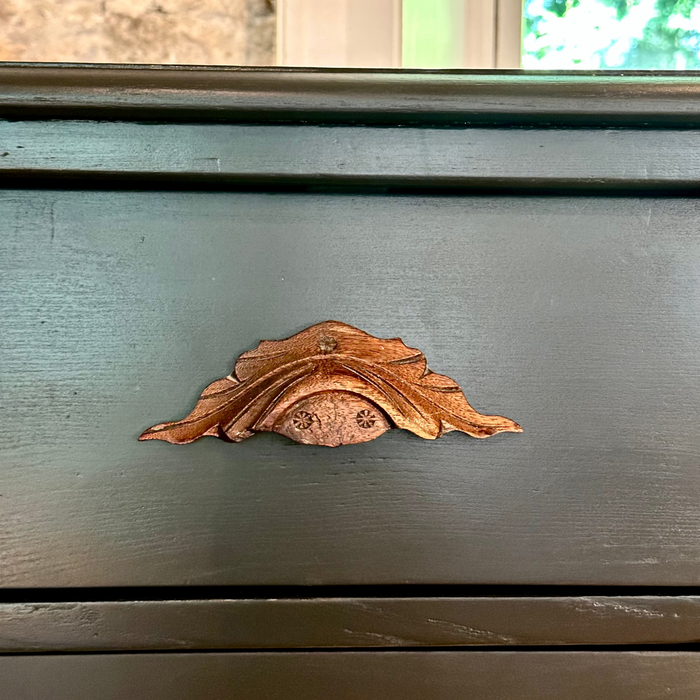 Decorative wood handle on a wooden surface with a mirror and window in the background.